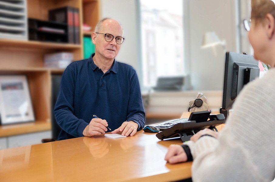 Dr. Grotkamp sitzt an einem Schreibtisch und schreibt auf einem Notizblock gegenüber einer Patientin.
